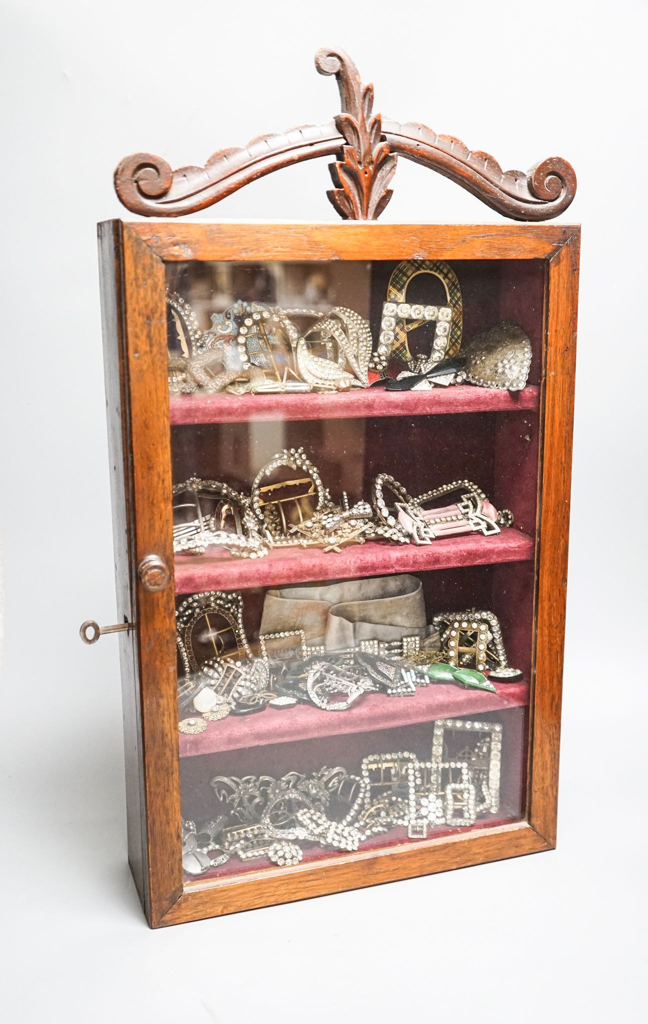 A large collection of 19th/20th century paste and enamel belt and shoe buckles and clips, contained in an oak display cabinet. 56cm